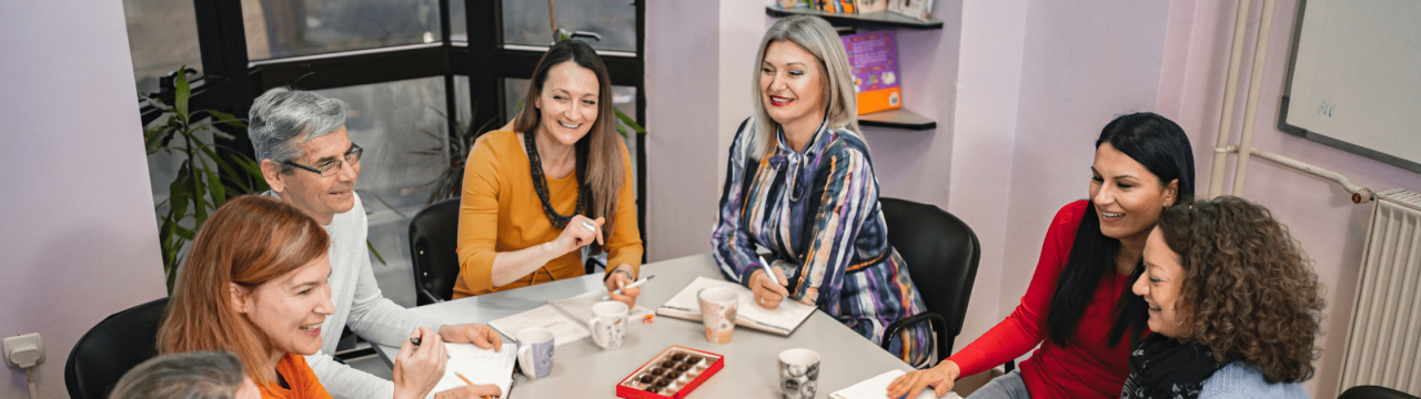 Group of teachers sat in a meeting around a large table, smiling
