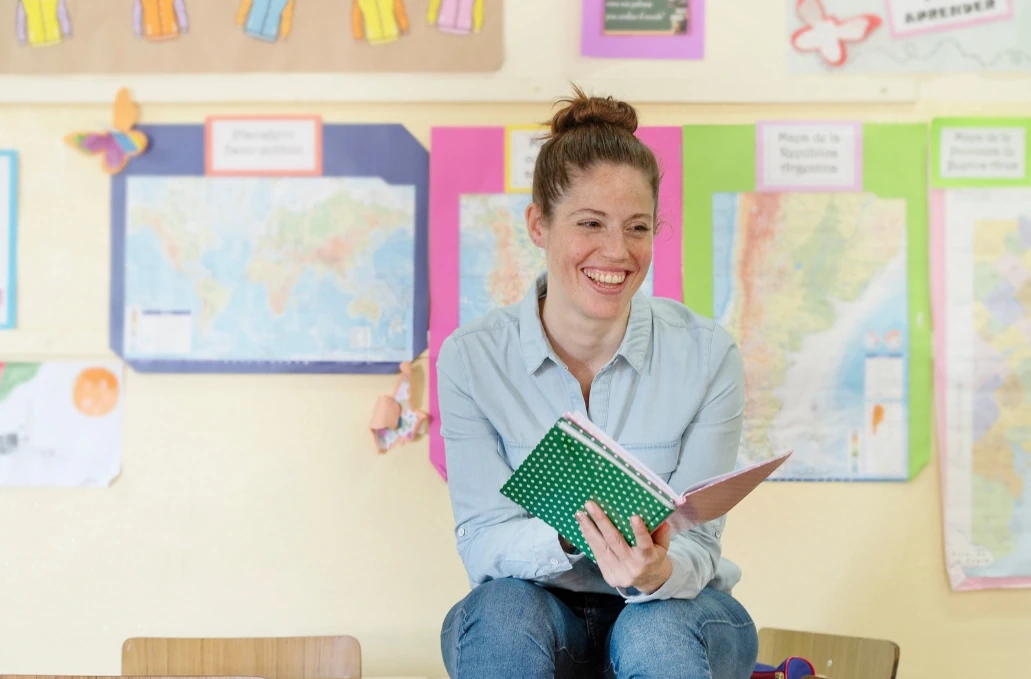 Young female teacher sits reading an exercise book in a classroom