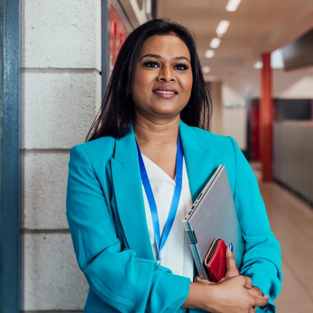 Smiling female teacher in a blue suit stood in hallway with a laptop